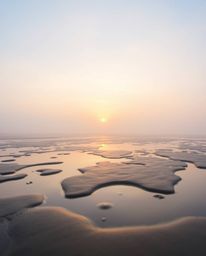 A dreamy photograph captures a beautiful sunset sky as it is mirrored in the tidal pools on a beach. The image is characteriz