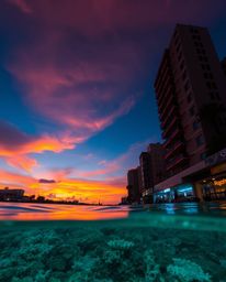 A candid street photography style image captures a colorful sky over a coral reef at low tide, blending urban spontaneity wit