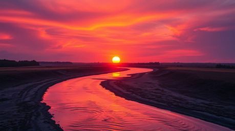 A breathtaking scene captures a winding river reflecting the dramatic orange-pink hues of the sunset sky, creating a vibrant 