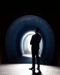 A high-resolution stock photo showcasing a person in a stylish suit standing at the edge of a tunnel, captivated by the light