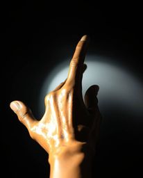 A captivating cast bronze hand, rendered with warm terracotta and a cool teal patina, extends towards a light source emerging