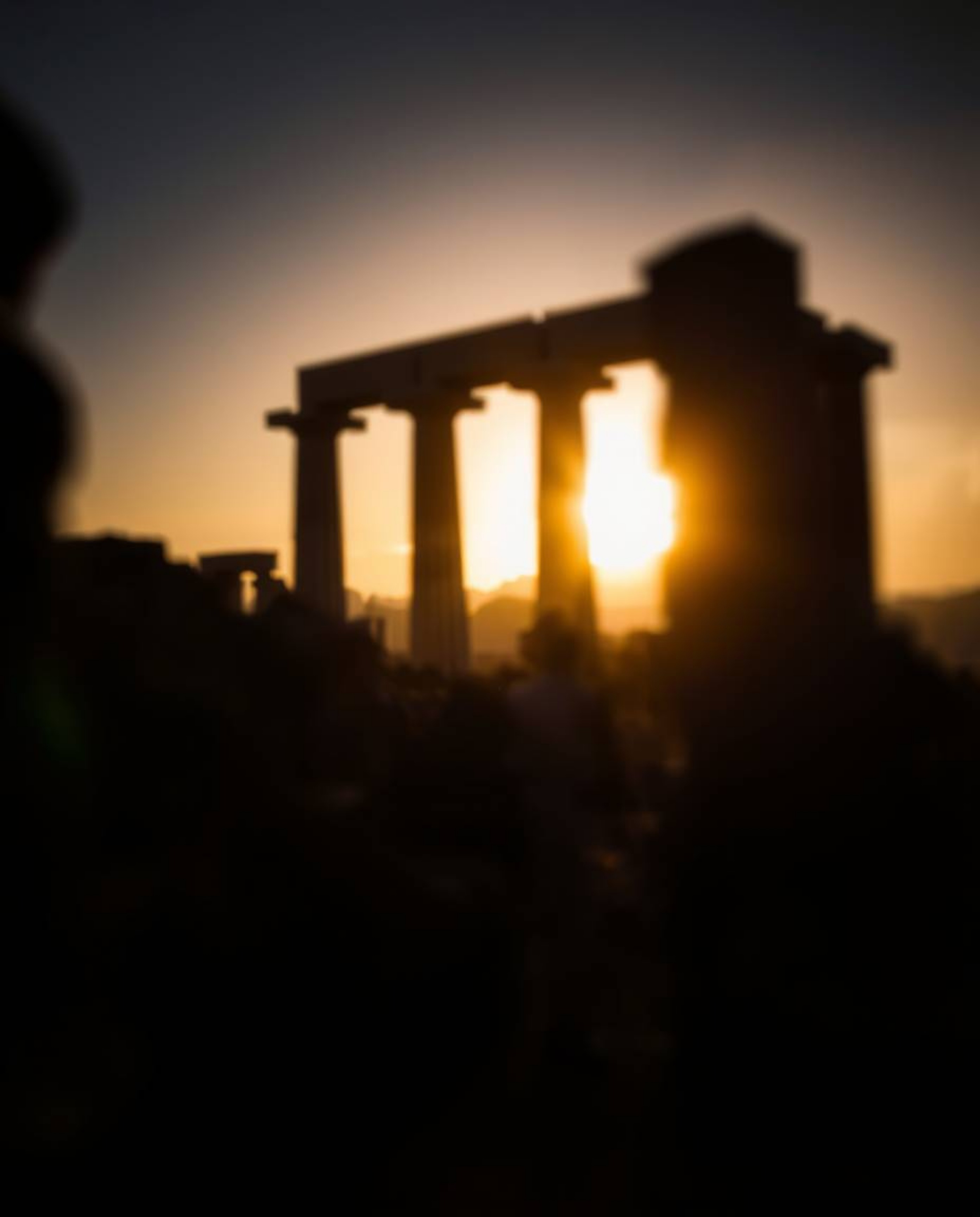 A blurred bokeh effect is created with high-contrast, low-key lighting as a sunset casts shadows through ancient stone ruins.