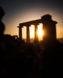A blurred bokeh effect is created with high-contrast, low-key lighting as a sunset casts shadows through ancient stone ruins.