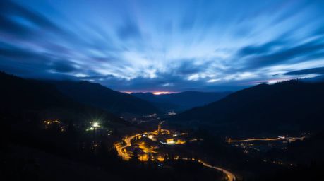 Capture the magic of a cozy village nestled in a valley under a vibrant, colorful sky with long exposure photography. This te