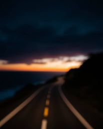 This image captures a sunset sky over a winding coastal highway with an intense jet black theme and a pronounced blurred boke