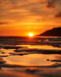 A high-resolution stock photo captures a tight close-up of a sunset sky mirrored in tidal pools on a beach. Shot during the w