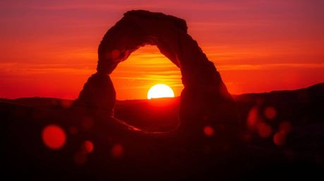 A captivating piece of warm, creative light art showcases a vibrant sunset viewed through a majestic desert rock arch.  The a