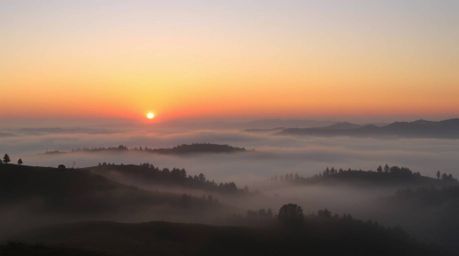 Capture the serene beauty of fog-covered hills bathed in the warm glow of a sunset. This image showcases a smooth gradient tr