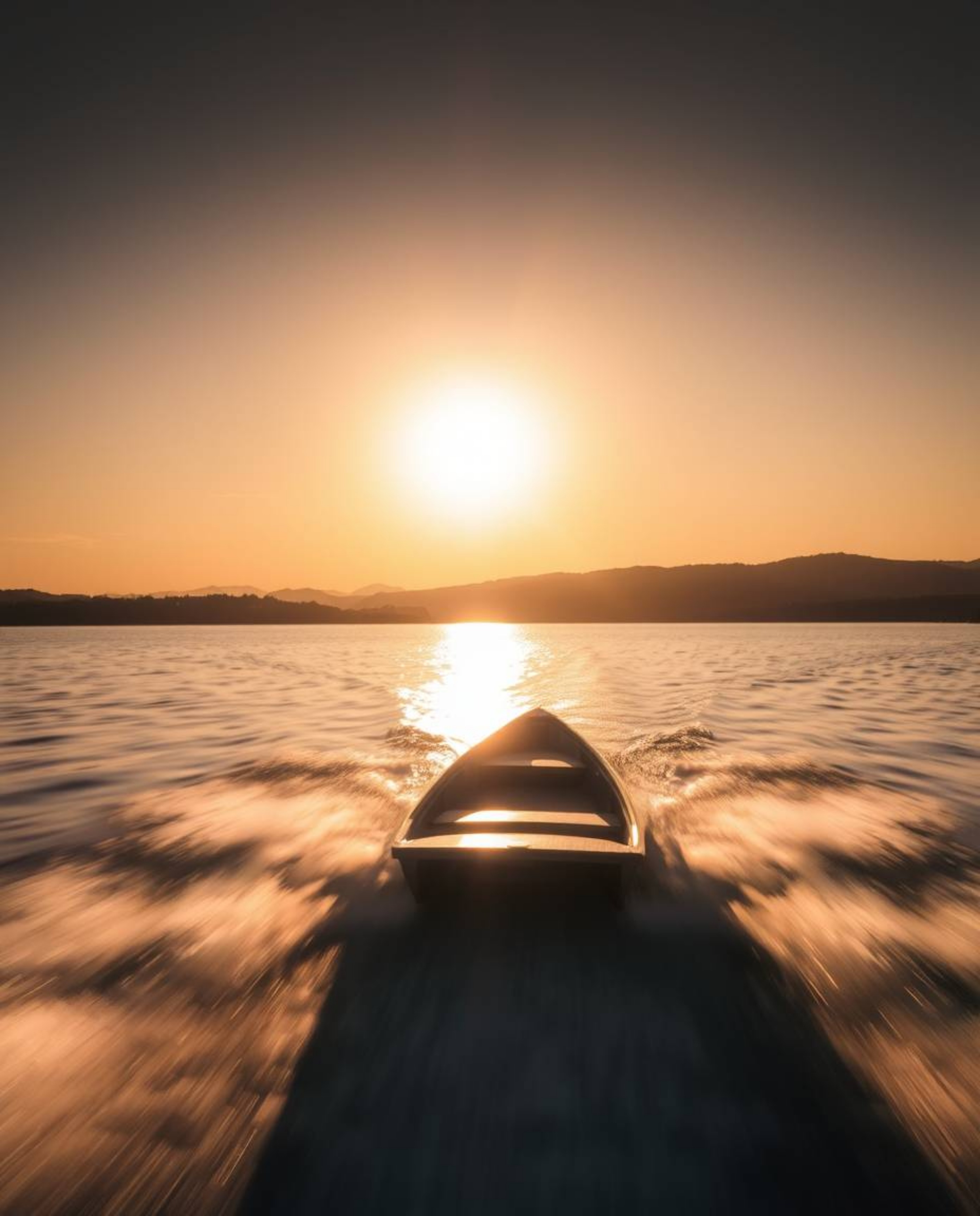 A photograph of a boat drifting on a sunset lake is captured with a long exposure, creating a stunning motion blur effect tha