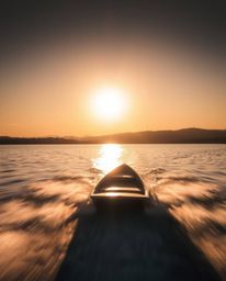 A photograph of a boat drifting on a sunset lake is captured with a long exposure, creating a stunning motion blur effect tha