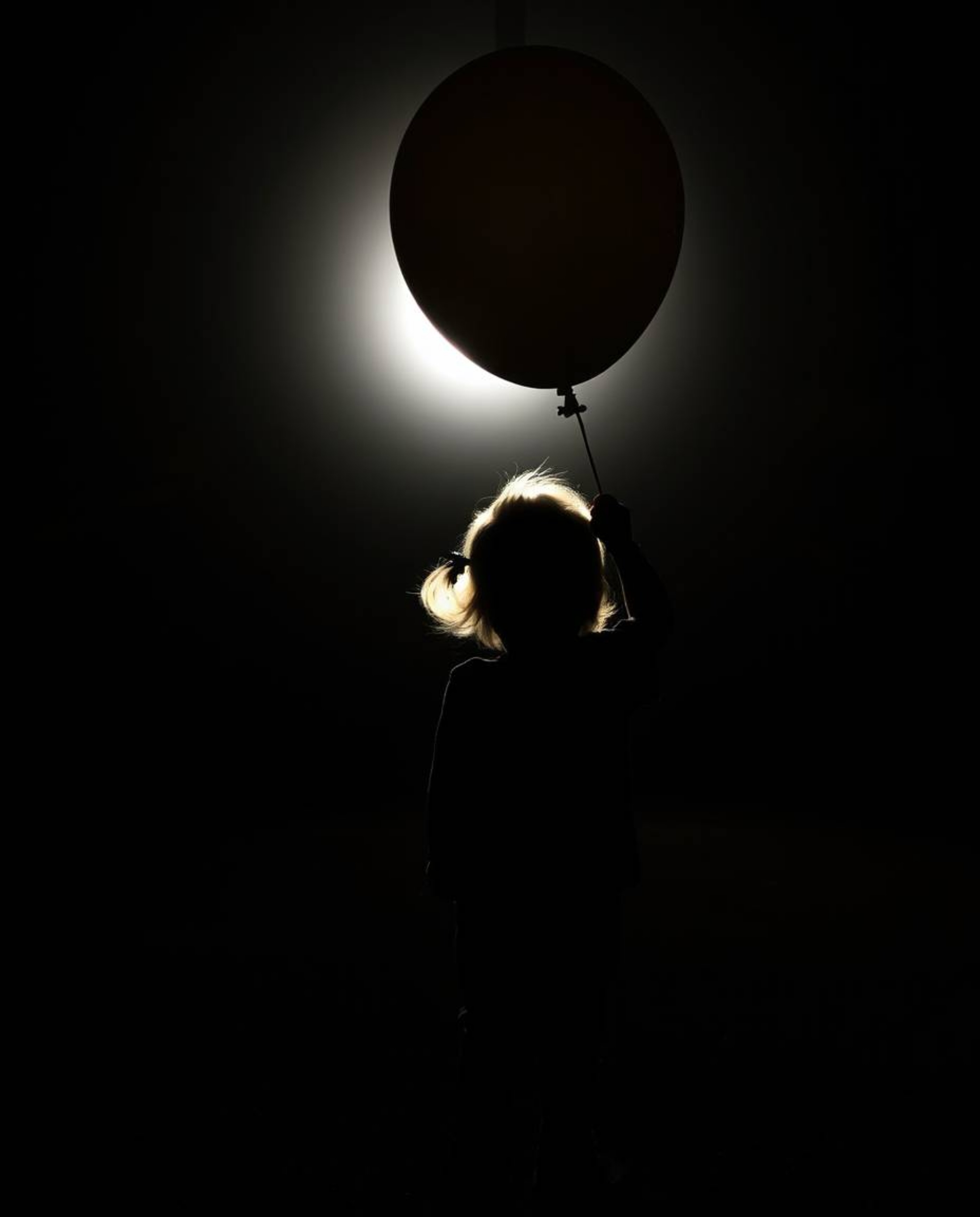 A captivating image of a child holding a balloon, silhouetted against a bright backlight. This visually striking photograph o
