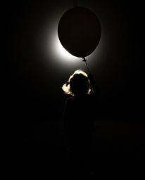 A captivating image of a child holding a balloon, silhouetted against a bright backlight. This visually striking photograph o