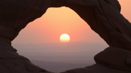A breathtaking cinematic photograph captures a vibrant sunset viewed through a majestic desert rock arch.  The image features