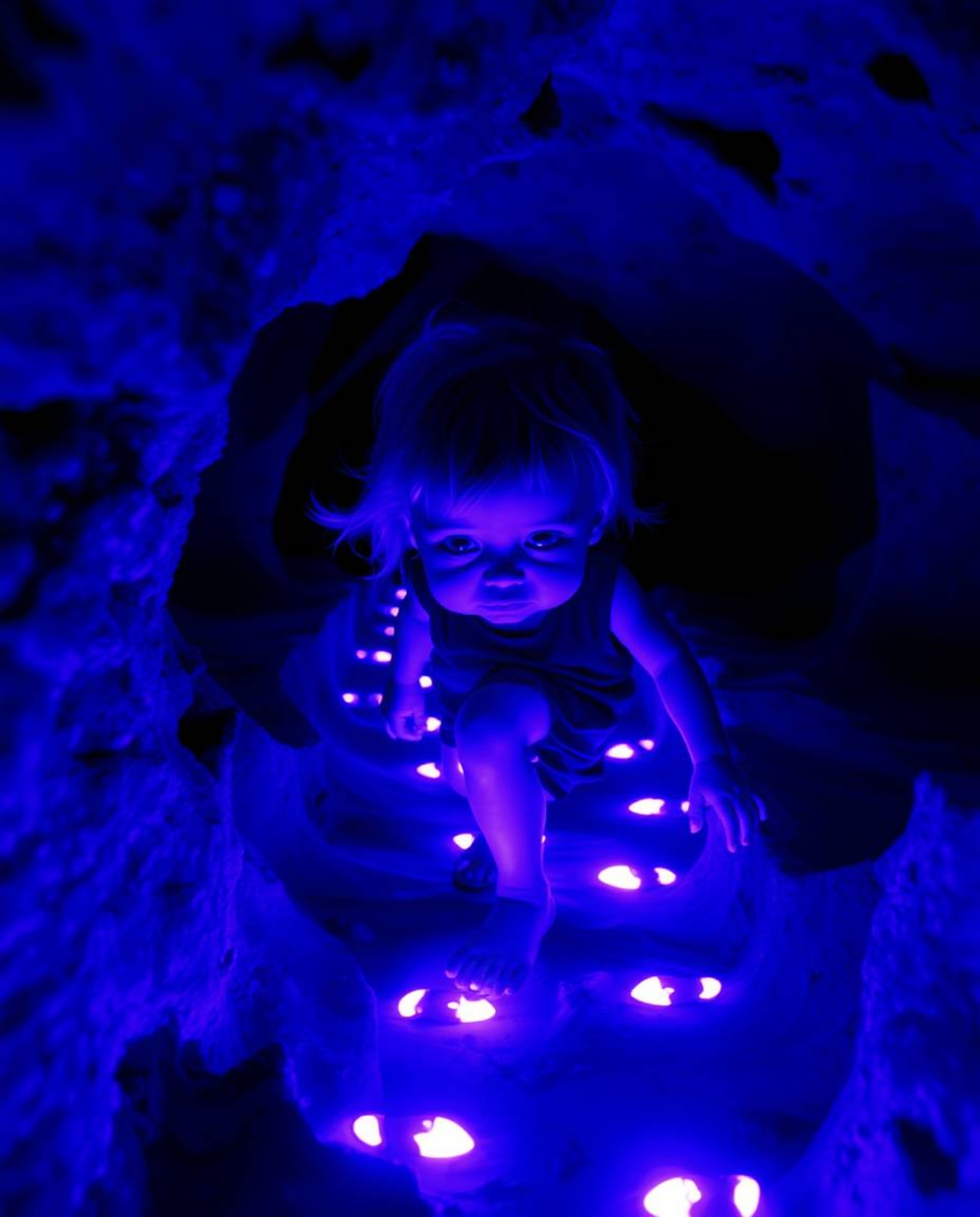A captivating ultraviolet light painting depicts a child with delicate features venturing into a cave, guided by glowing purp