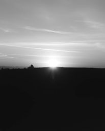 A classic black and white photograph capturing the serene beauty of a sunrise over a war-torn landscape. The image conveys gr