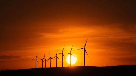 A captivating high-resolution photograph showcasing the powerful imagery of a sunset silhouetting a row of wind turbines atop