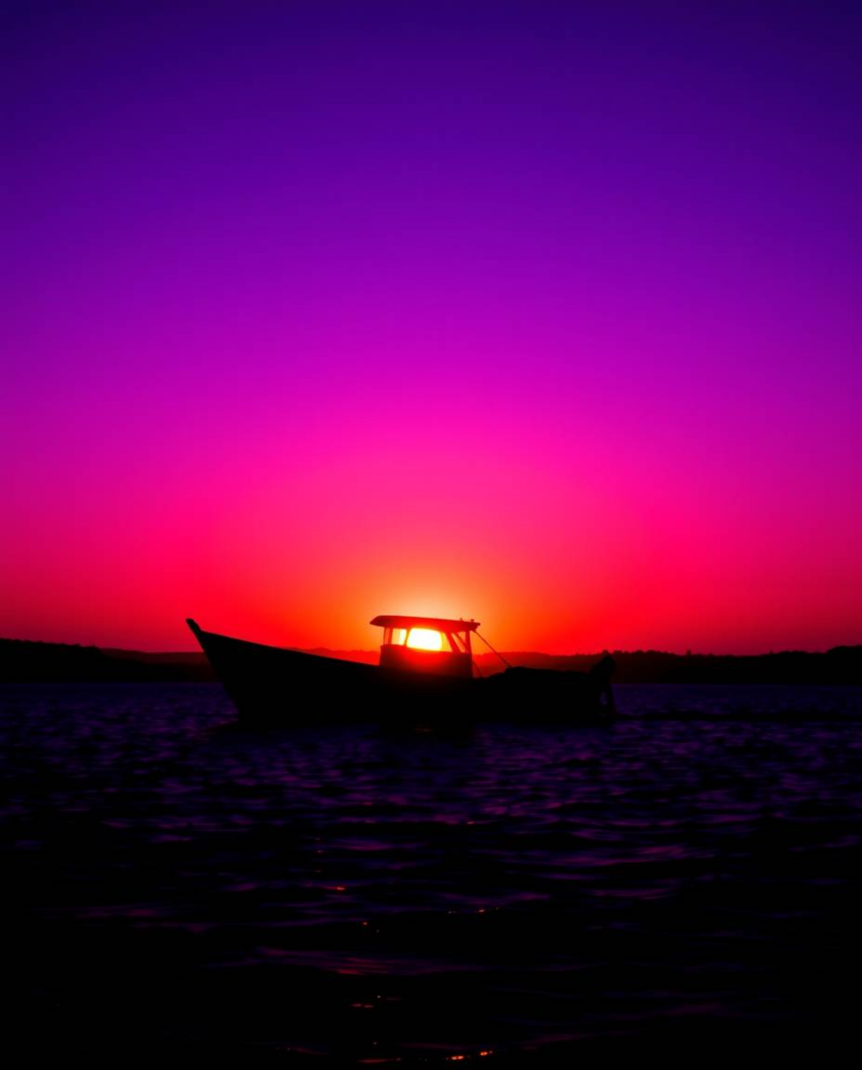 A silhouetted boat is depicted drifting on a lake at sunset, created by a striking backlighting effect. The scene is saturate