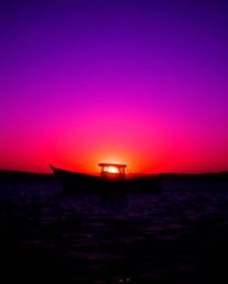 A silhouetted boat is depicted drifting on a lake at sunset, created by a striking backlighting effect. The scene is saturate