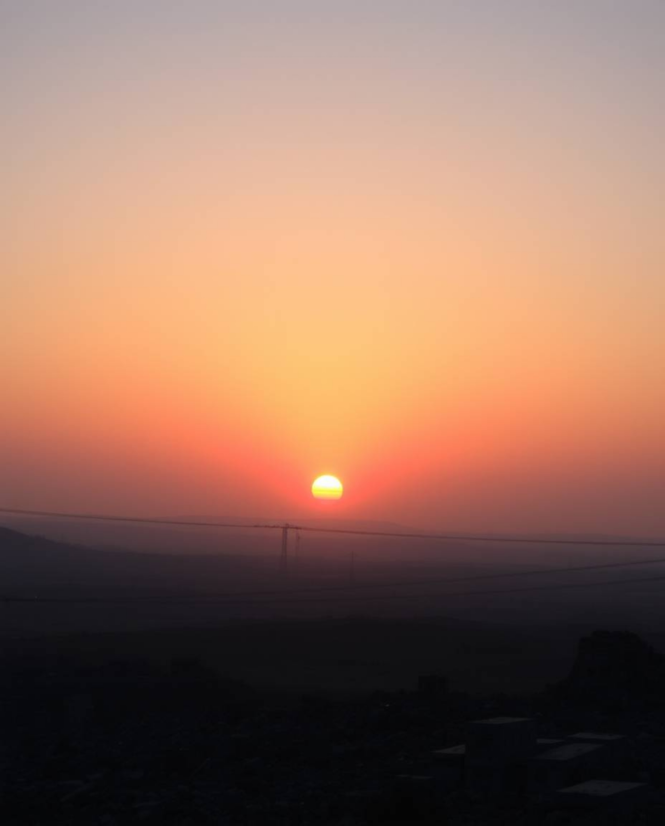 A captivating image depicting a sunrise over a war-torn landscape.  Iridescent colors paint the sky, casting soft light and d