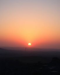A captivating image depicting a sunrise over a war-torn landscape.  Iridescent colors paint the sky, casting soft light and d