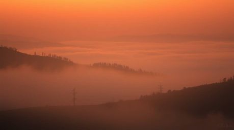 This image captures the serene beauty of fog-covered hills bathed in the warm glow of sunset. The low contrast and soft light