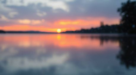 Capture the serene beauty of a lake reflecting a vivid sunset with a stunning bokeh effect.  This image showcases smooth grad