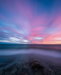 A long exposure photograph captures a split colorful sky over a coral reef at low tide. The composition is defined by bold se