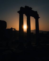 A strong, moody style image depicting a sunset casting shadows through ancient stone ruins. The scene is characterized by hig