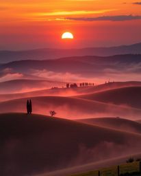 This is a high-resolution, professional-quality stock photo capturing a sunset over the misty, rolling hills of Tuscany. The 
