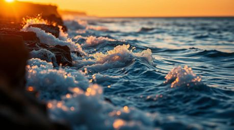 A stunning macro photograph captures waves crashing against cliffs during a vibrant sunset, showcasing iridescent colors and 