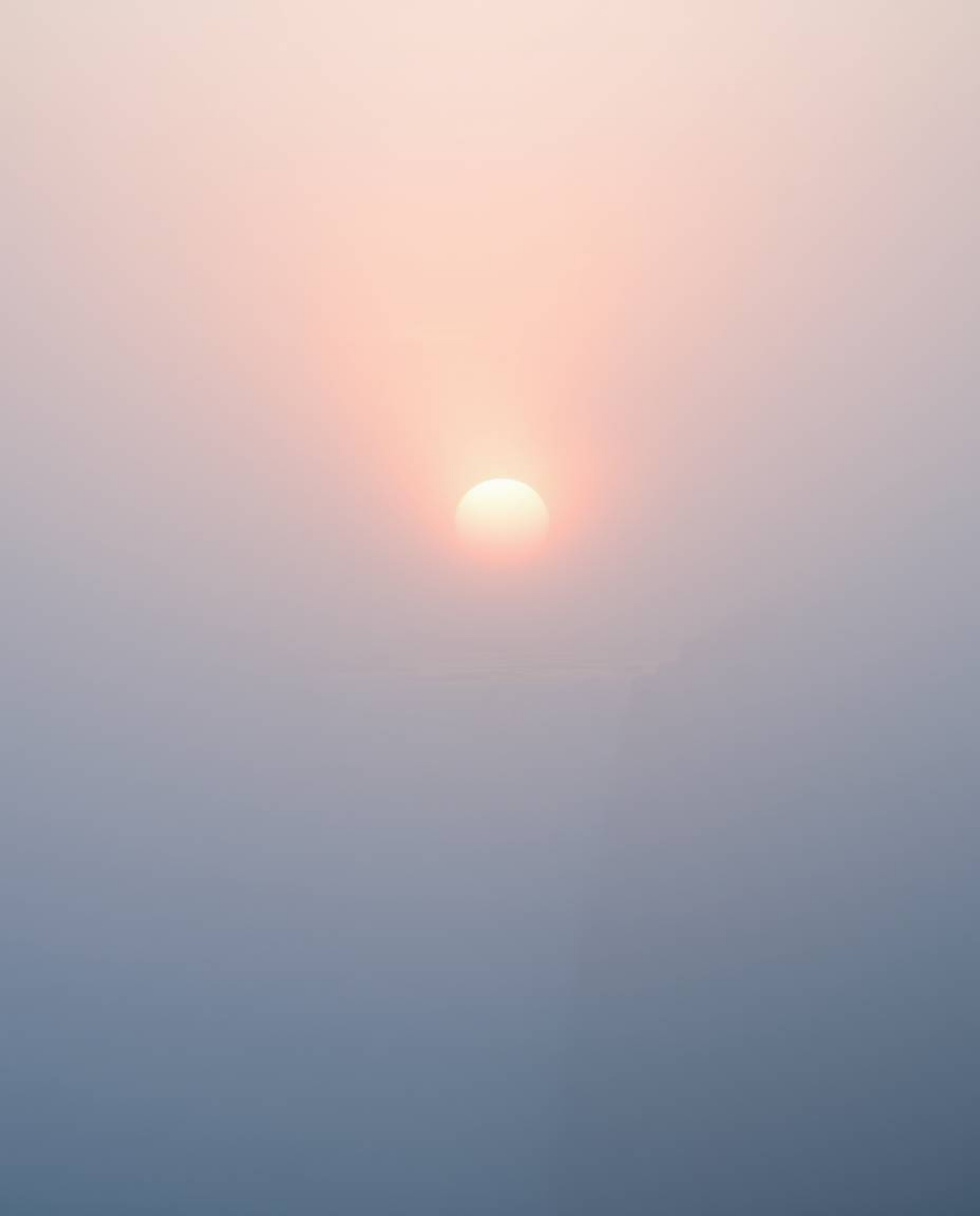 Thick fog and soft pastel colors characterize this scene of a sun setting behind a dramatic waterfall. The overall effect is 