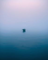 A boat drifts on a lake at sunset, the scene rendered with a cool color palette and blurred bokeh effect, enhancing the low v