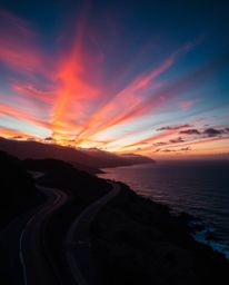 This artwork depicts a sunset sky over a winding coastal highway, rendered with a dramatic contrast of intense jet black and 