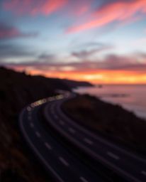 A captivating photo captures a sunset sky over a winding coastal highway, distinguished by a beautiful blurred bokeh effect a