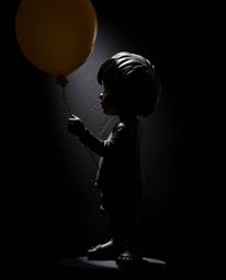 A striking piece of sculptural clay art depicts a child with dark skin holding a balloon.  Intense backlighting creates a dra