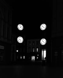A captivating black and white photograph showcasing an empty town square, punctuated by the ticking of clocks. The image evok