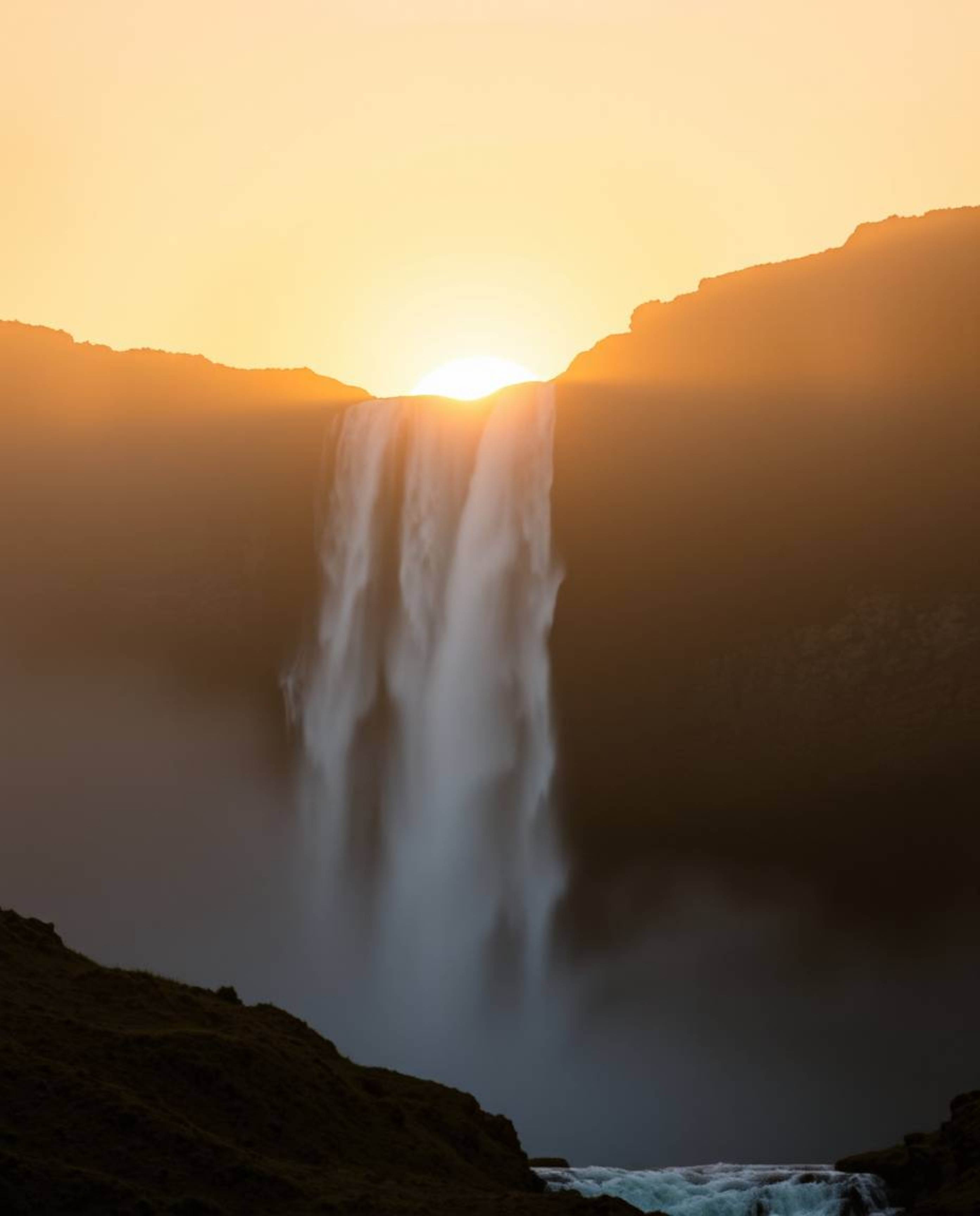 This artwork captures a stunning sunset behind a dramatic waterfall, featuring beautiful volumetric lighting and natural eart