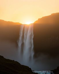 This artwork captures a stunning sunset behind a dramatic waterfall, featuring beautiful volumetric lighting and natural eart