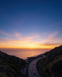 This artwork offers a high-angle perspective of a sunset sky over a winding coastal highway. The scene is characterized by a 