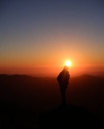 Behold a striking scene of a silhouetted figure set against a breathtaking sunset from a high alpine peak. This image is char