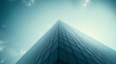 This image captures a modern glass building appearing to dissolve into the sky, shot from a high-angle perspective with high-
