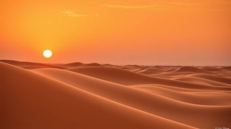 A stunning architectural color photograph captures a vibrant sunset over golden desert dunes.  The image boasts sharp lines, 
