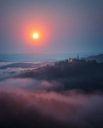 This is an ethereal and spiritual depiction of a sunset over the misty, rolling hills of Tuscany. The artwork evokes a mystic