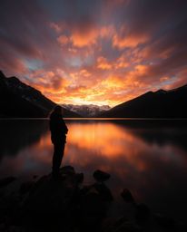 A long exposure photograph captures the reflections of fiery clouds in a mountain lake, utilizing silhouetted backlighting fr