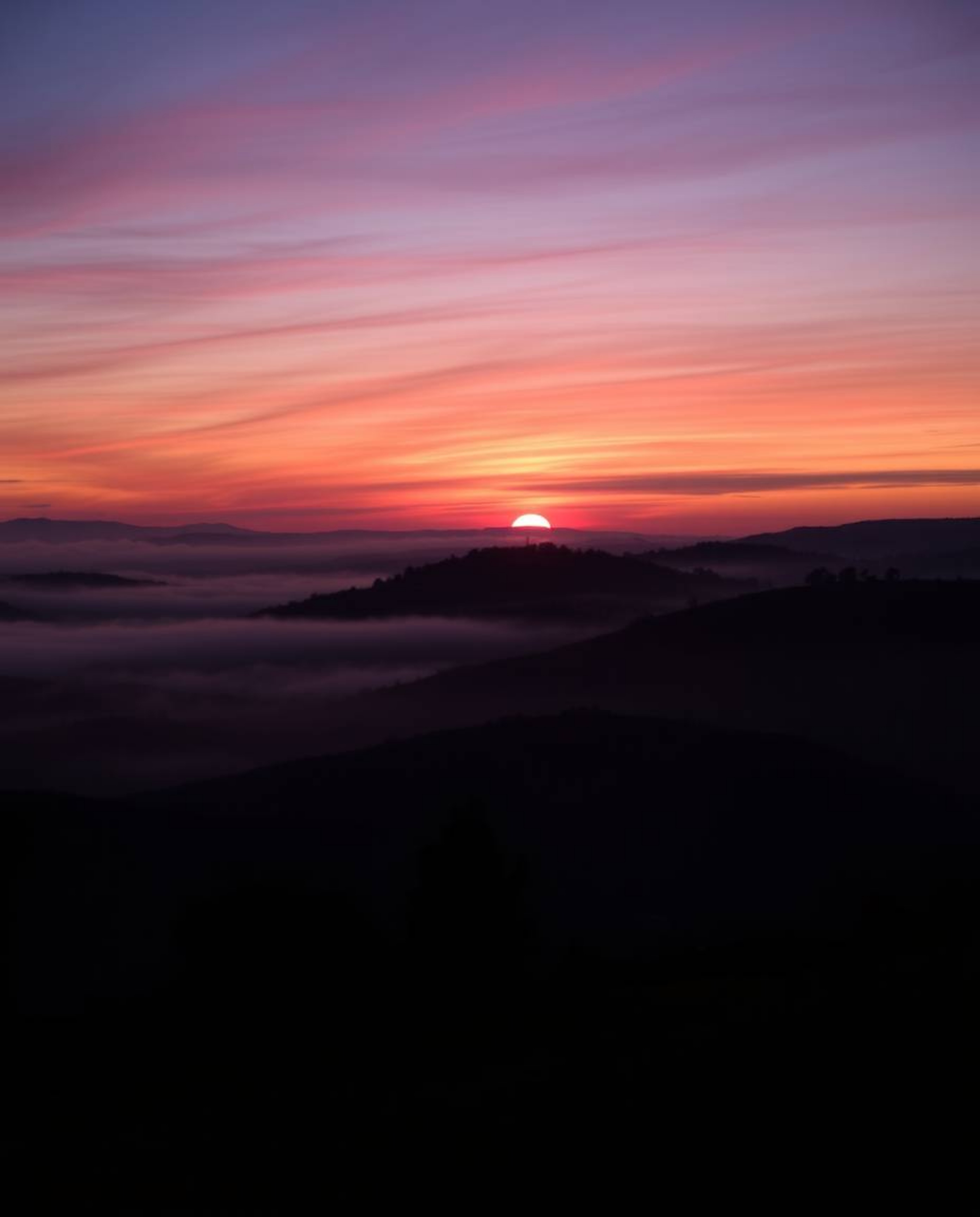 A sophisticated, elegant long-exposure photograph showcasing a Tuscan sunset over misty hills, rich burgundy and deep blue hu