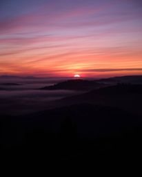 A sophisticated, elegant long-exposure photograph showcasing a Tuscan sunset over misty hills, rich burgundy and deep blue hu