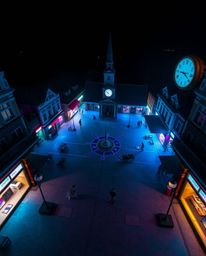Capture the surreal beauty of an empty town square bathed in glowing, bioluminescent colors.  The scene features ticking cloc