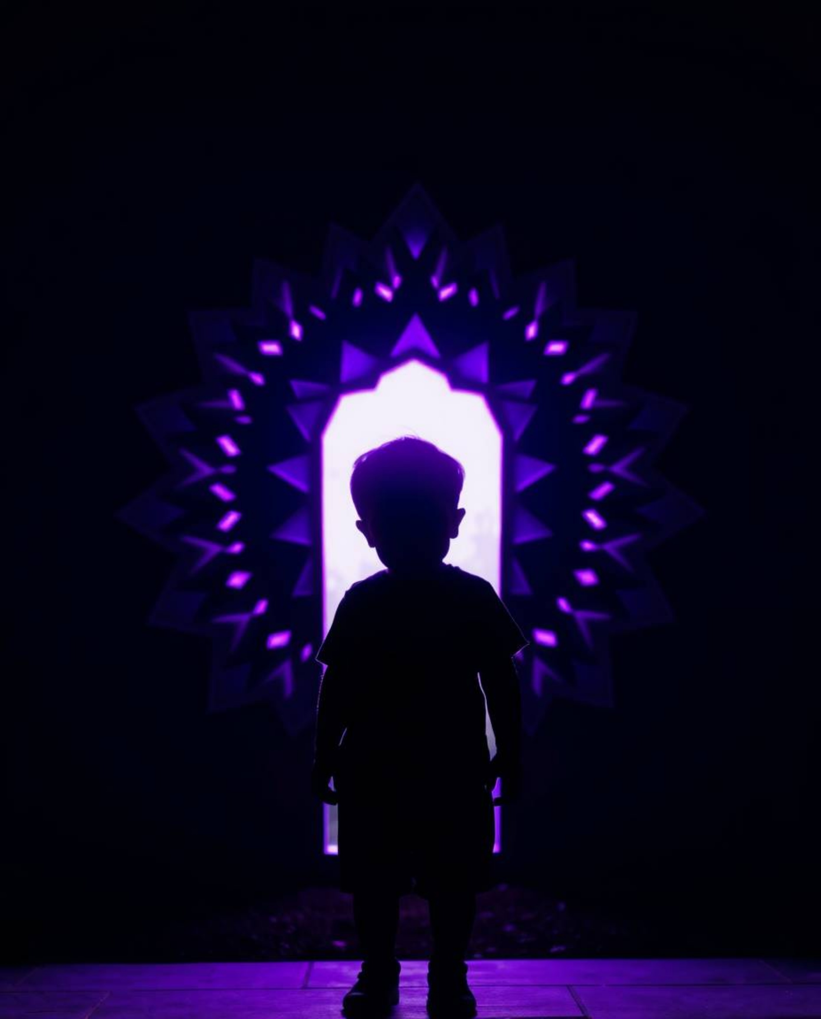 A captivating image depicts a child silhouetted against a vibrant, deep ultraviolet portal in their backyard. The scene is r