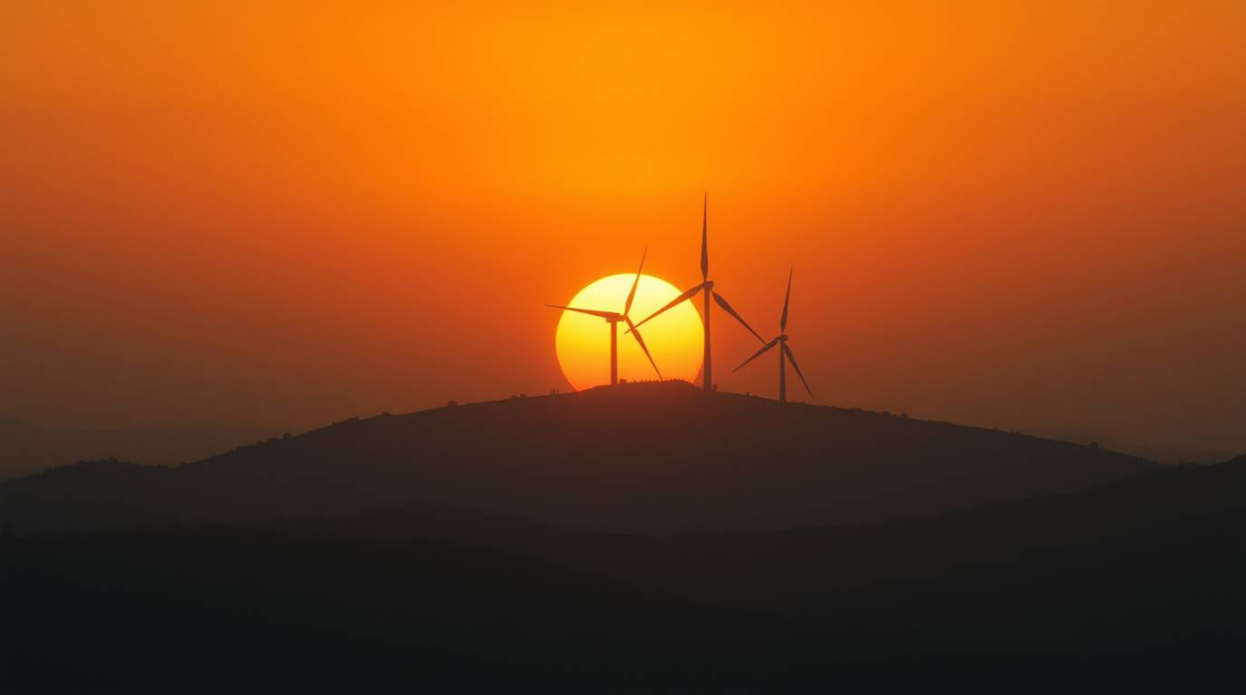 Experience an epic cinematic scene featuring a breathtaking sunset behind a row of wind turbines on a hill. This image evokes