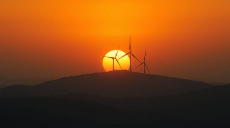 Experience an epic cinematic scene featuring a breathtaking sunset behind a row of wind turbines on a hill. This image evokes